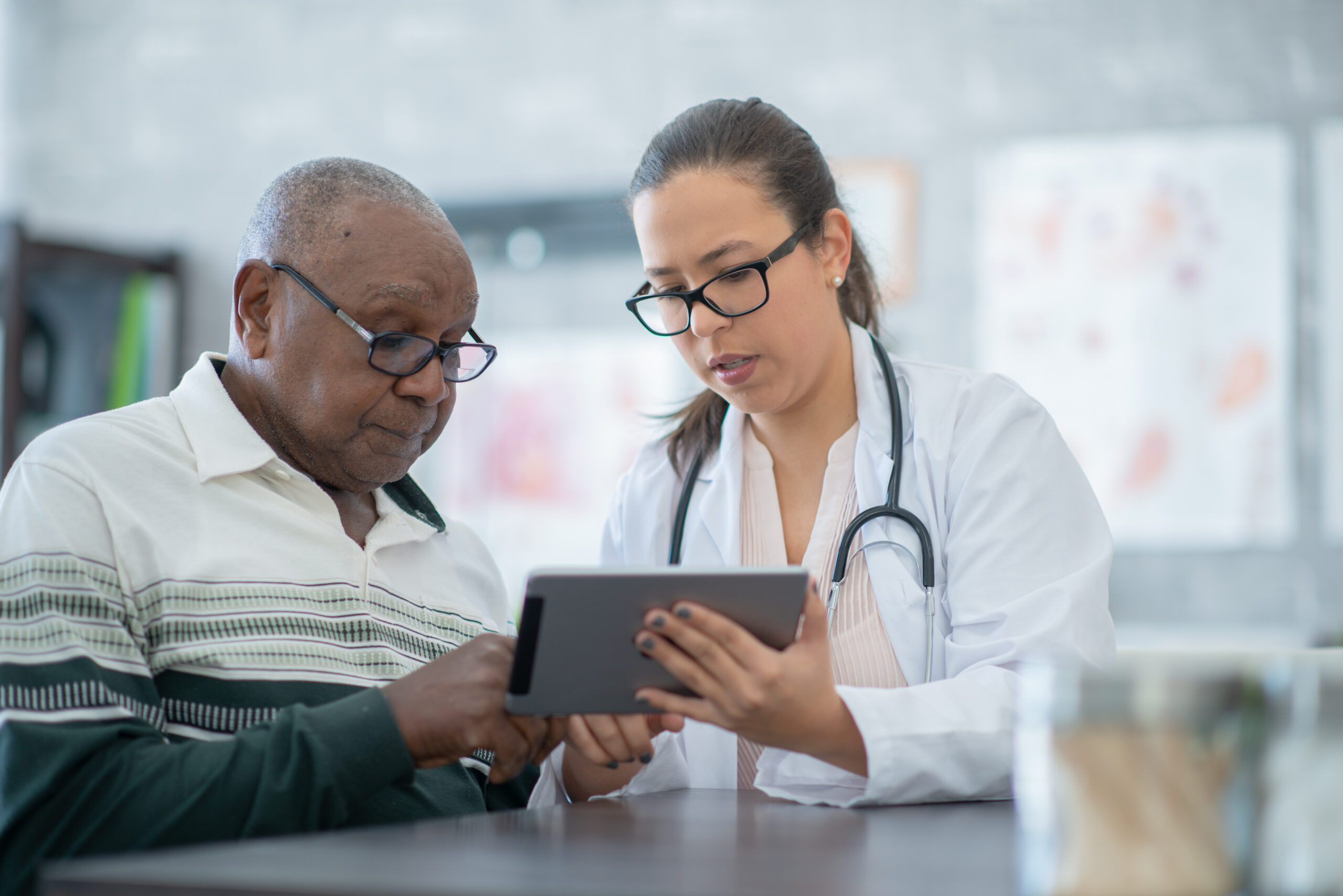 A Hispanic female doctor sits next to her patient at her office to discuss some test results. Her patient is a senior African American male.